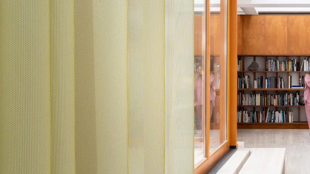 Acoustic Vescom Formoza sheer curtain with a green vertical accent yarn, providing transparency in a library setting.
