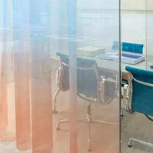 Transparent Vescom Airy curtain with a blue and orange gradient, creating a soft color wash in a modern office space.