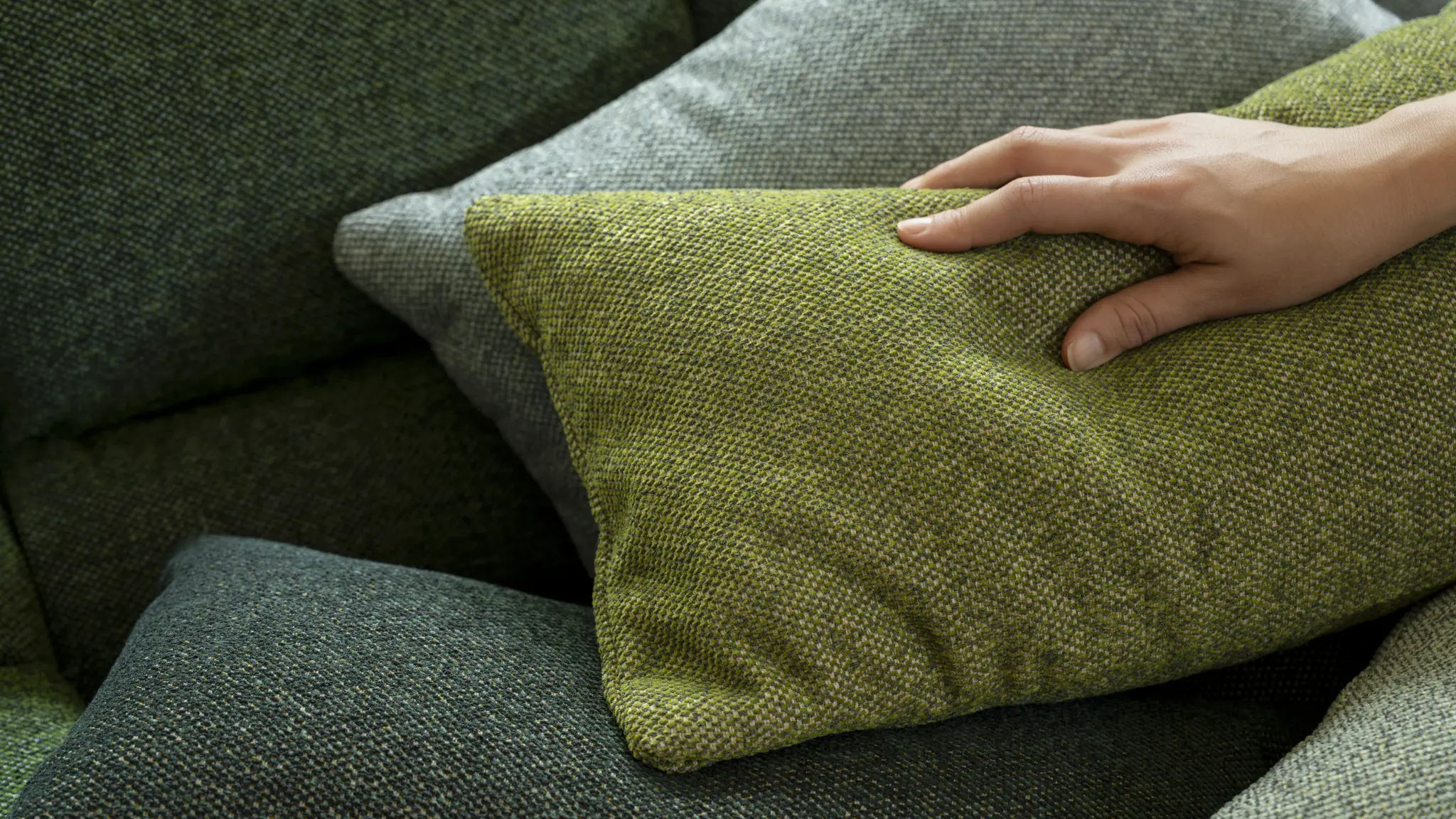A hand feels the soft, woolly texture of green Vescom Bosco upholstery.