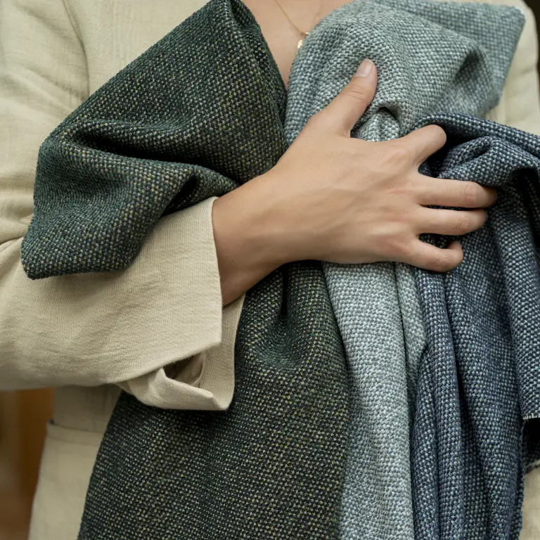 A hand folds green Vescom Bosco upholstery to show its fluid, flexible quality.