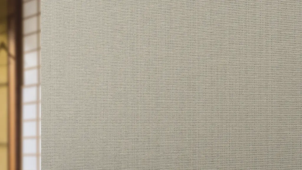 Vescom Birch woven textile wallcovering with subtle slub texture and architectural grid behind a wooden bowl on a table