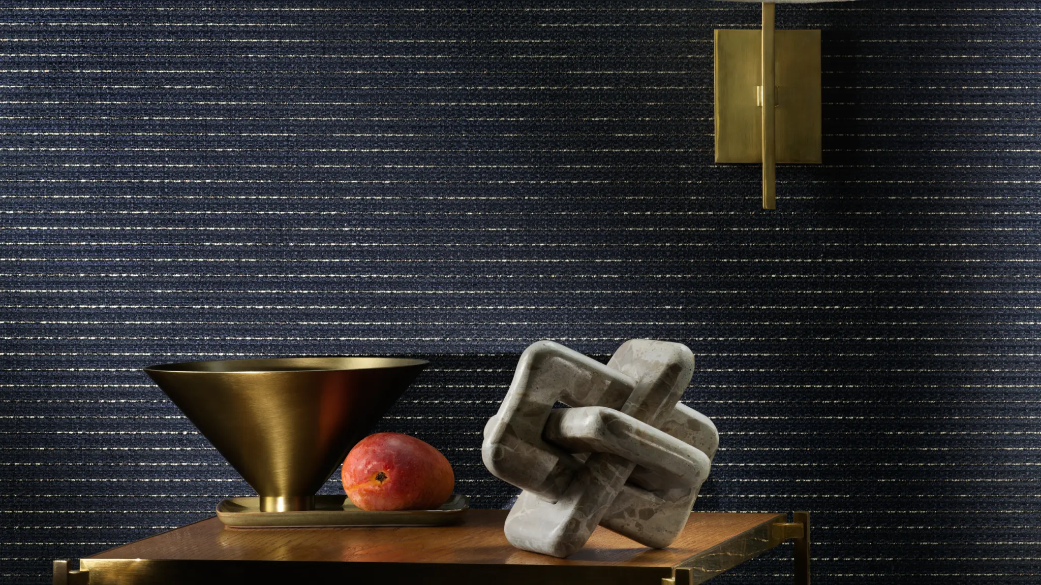 escom Eldor textile wallcovering with a refined woven structure and subtle metallic thread, creating a softly radiant surface, shown on interior walls in a styled setting with decorative objects and wall lighting