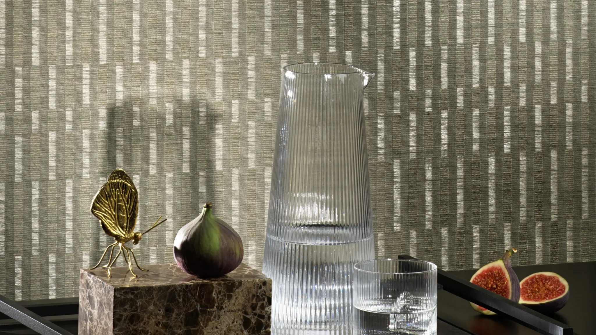 Vescom Fiero textile wallcovering featuring a refined vertical pattern, styled interior scene with glass carafe, marble object and figs