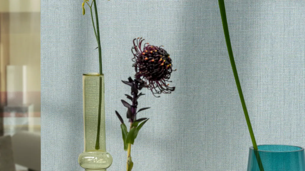 Vescom Gemstone woven textile wallcovering with small grid texture behind colourful glass vases and flowers