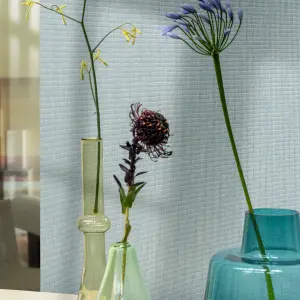 Vescom Gemstone woven textile wallcovering with small grid texture behind colourful glass vases and flowers