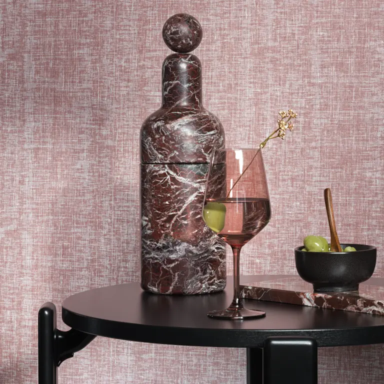 Vescom Ludi textile wallcovering with a fine airy weave inspired by linen, creating a light textured surface, shown on interior walls behind a styled table setting with a marble bottle, wine glass and olives