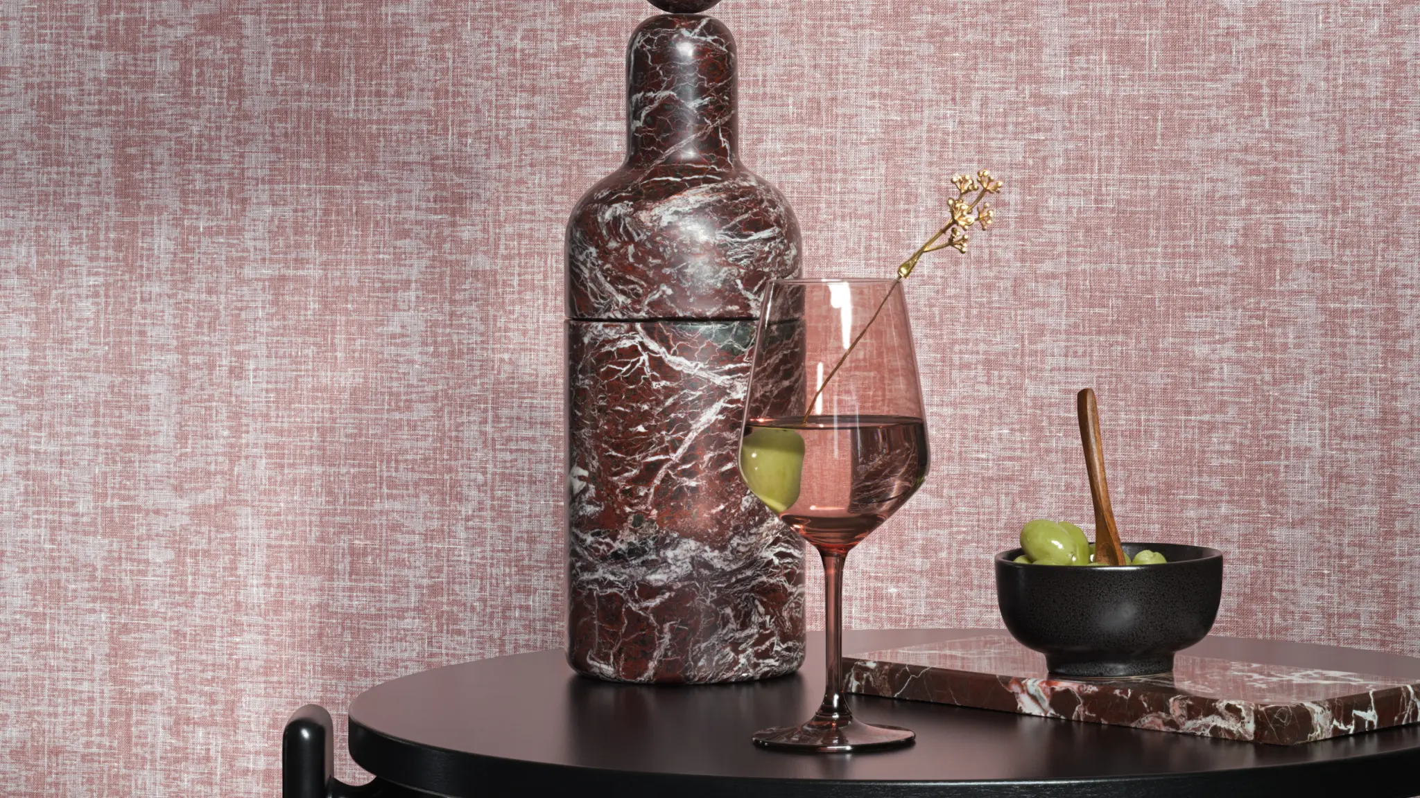 Vescom Ludi textile wallcovering with a fine airy weave inspired by linen, creating a light textured surface, shown on interior walls behind a styled table setting with a marble bottle, wine glass and olives