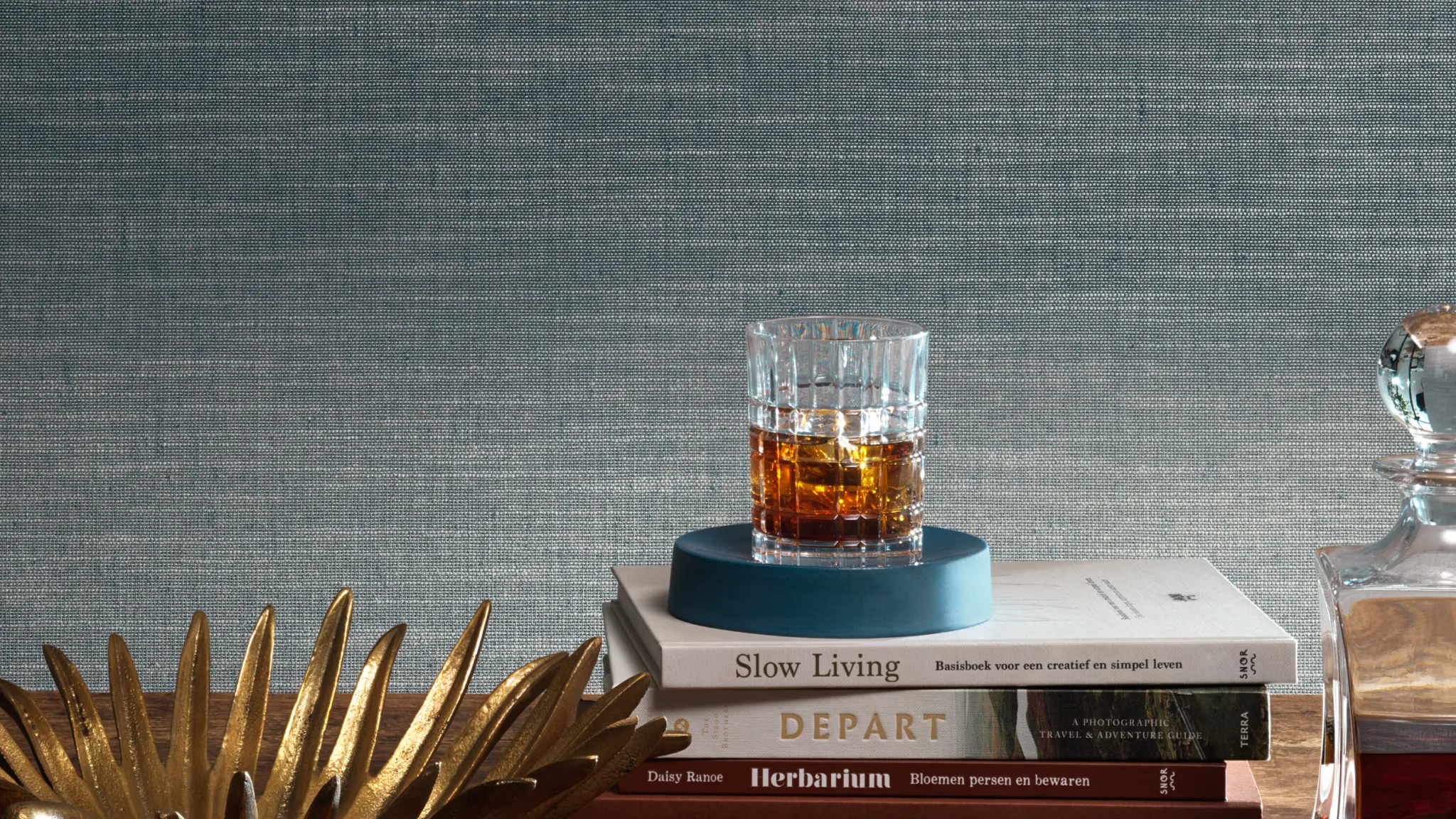 “Vescom Nivelis textile wallcovering with a two-tonal woven horizontal structure and subtle melange effect, shown on interior walls behind a styled table with books, glassware and decorative objects