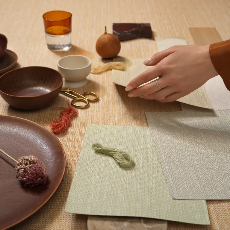 Vescom Sisu textile wallcovering with a structured herringbone weave, creating a measured and rhythmic surface, shown with material samples in a styled interior setting