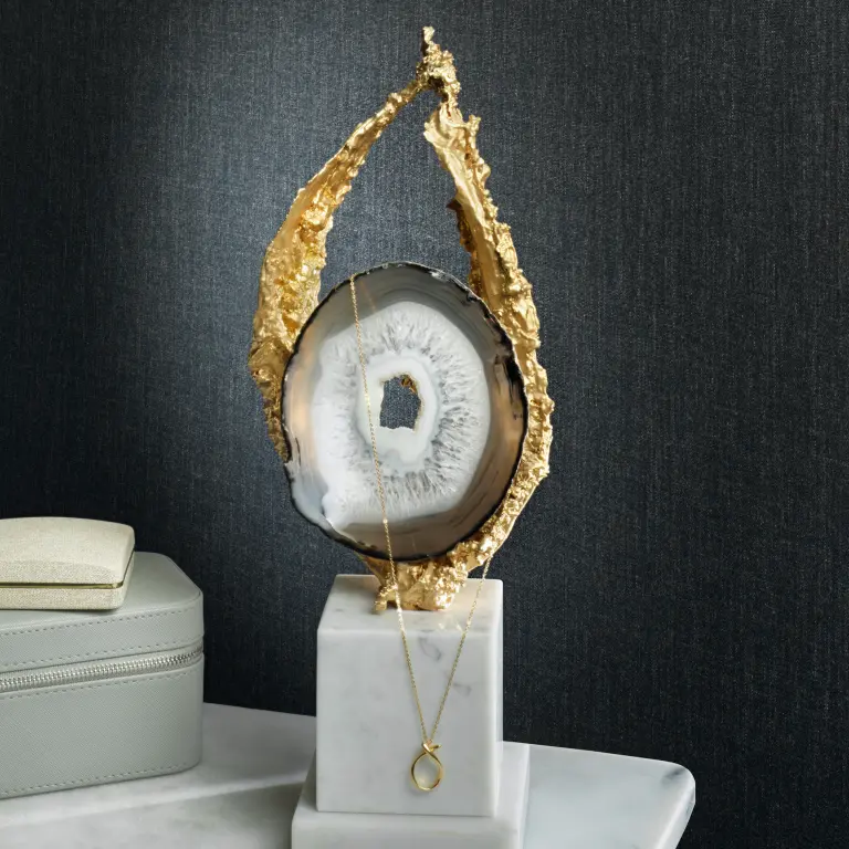 “Vescom Solene textile wallcovering with a tailored wool-inspired weave creating a poised and understated surface, shown on interior walls behind a styled display with a decorative stone object and jewelry