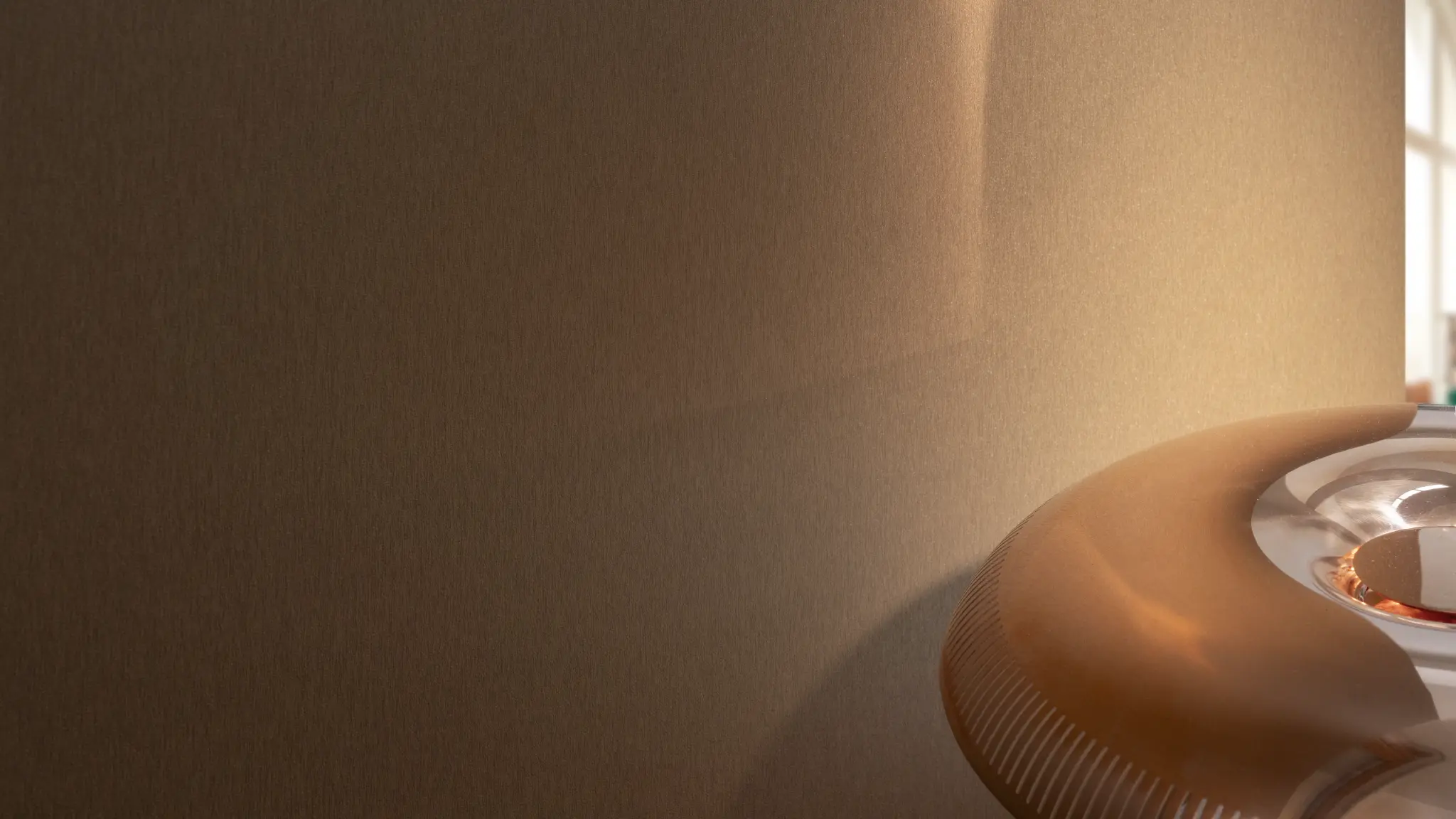 Vescom Stellar vinyl wallcovering in a warm interior, showing a brushed metallic surface with soft light reflection.